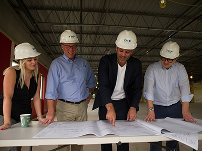 Moshe and group wearing hard hats looking at blueprints